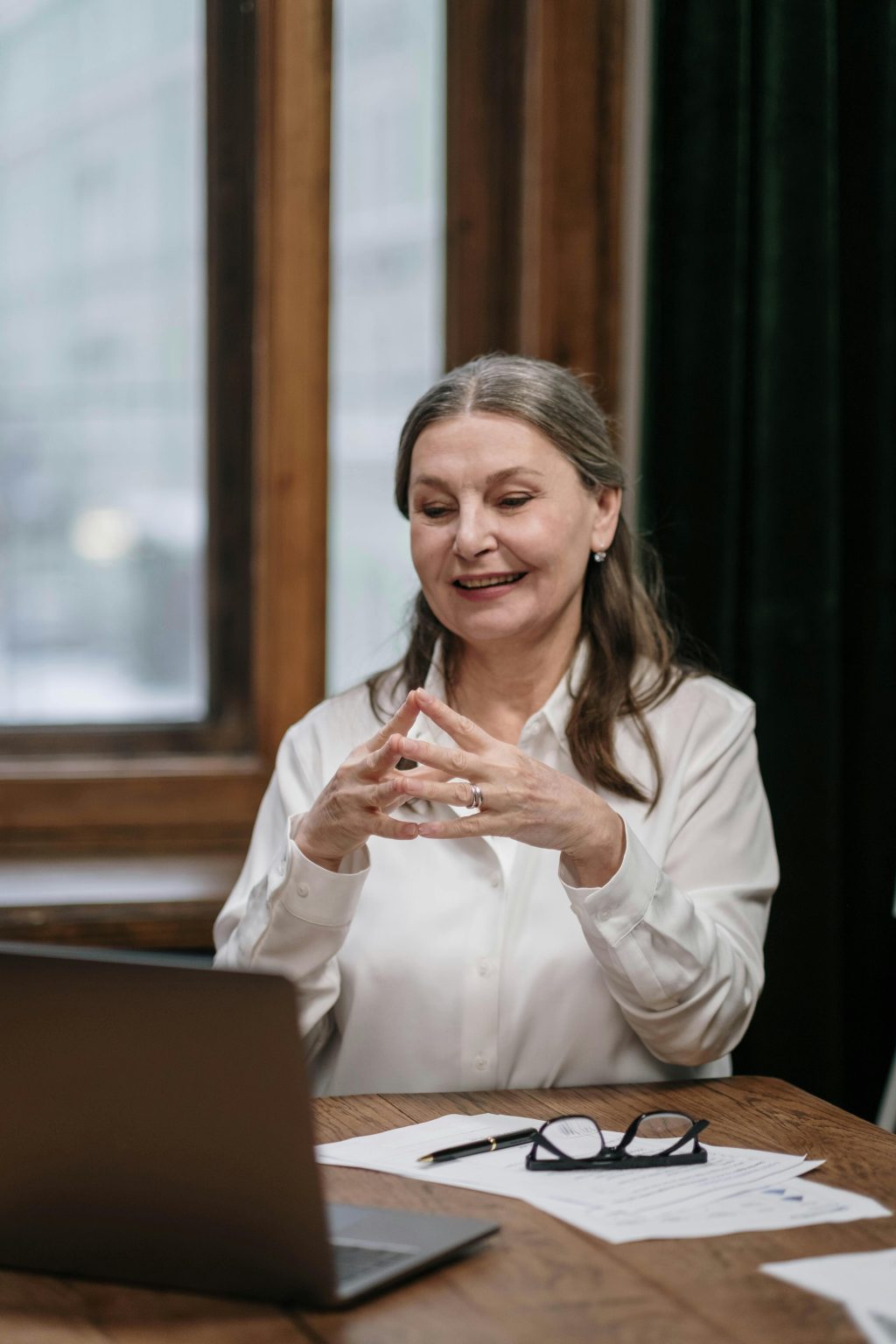 Senior Caucasian woman with grey hair teaching online course via laptop, smiling and engaged.