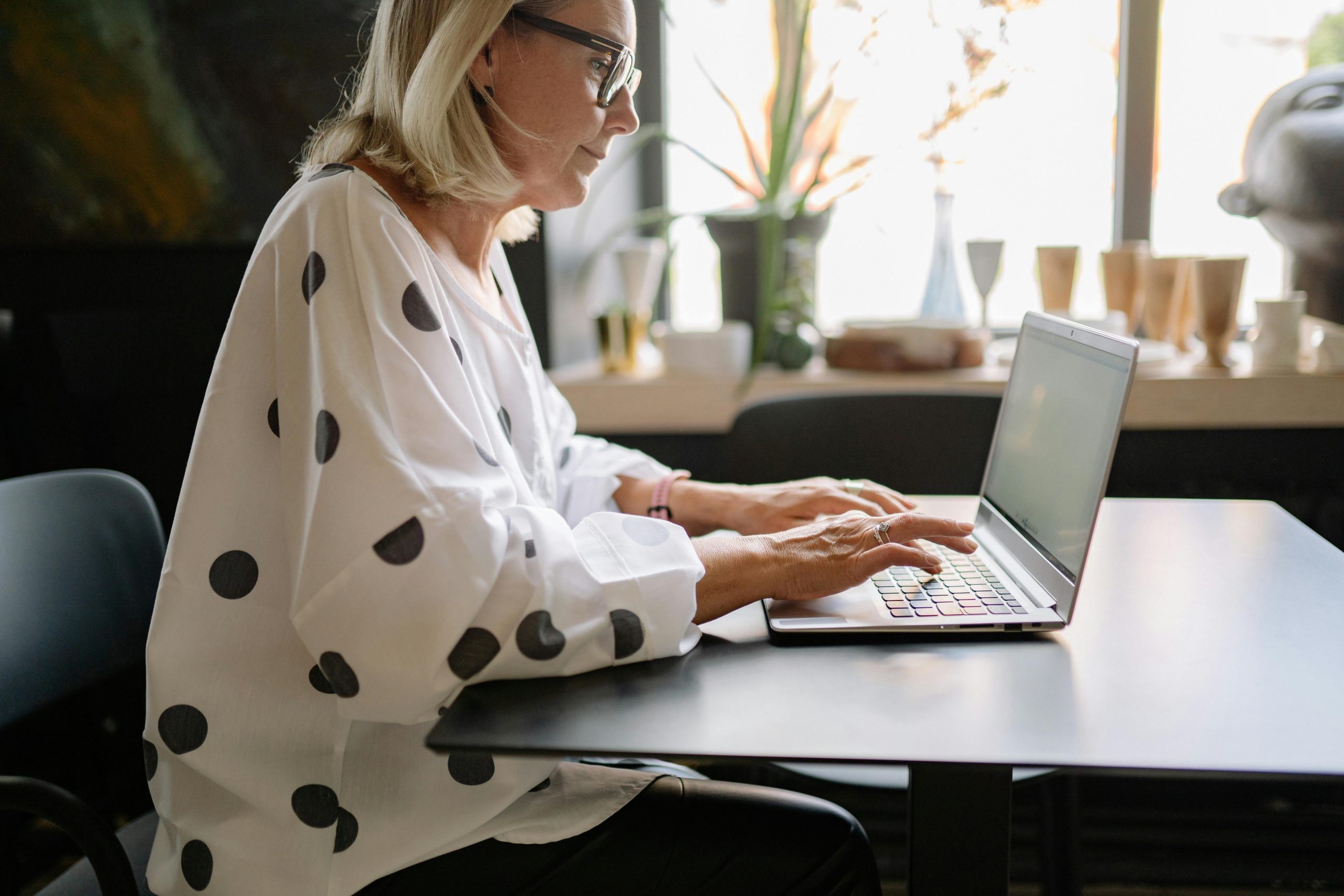 A professional woman working on a laptop at a desk in a well-lit office setting.